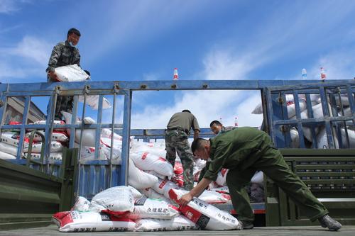 图为：武装部人员帮助贫困户装卸化肥的场景