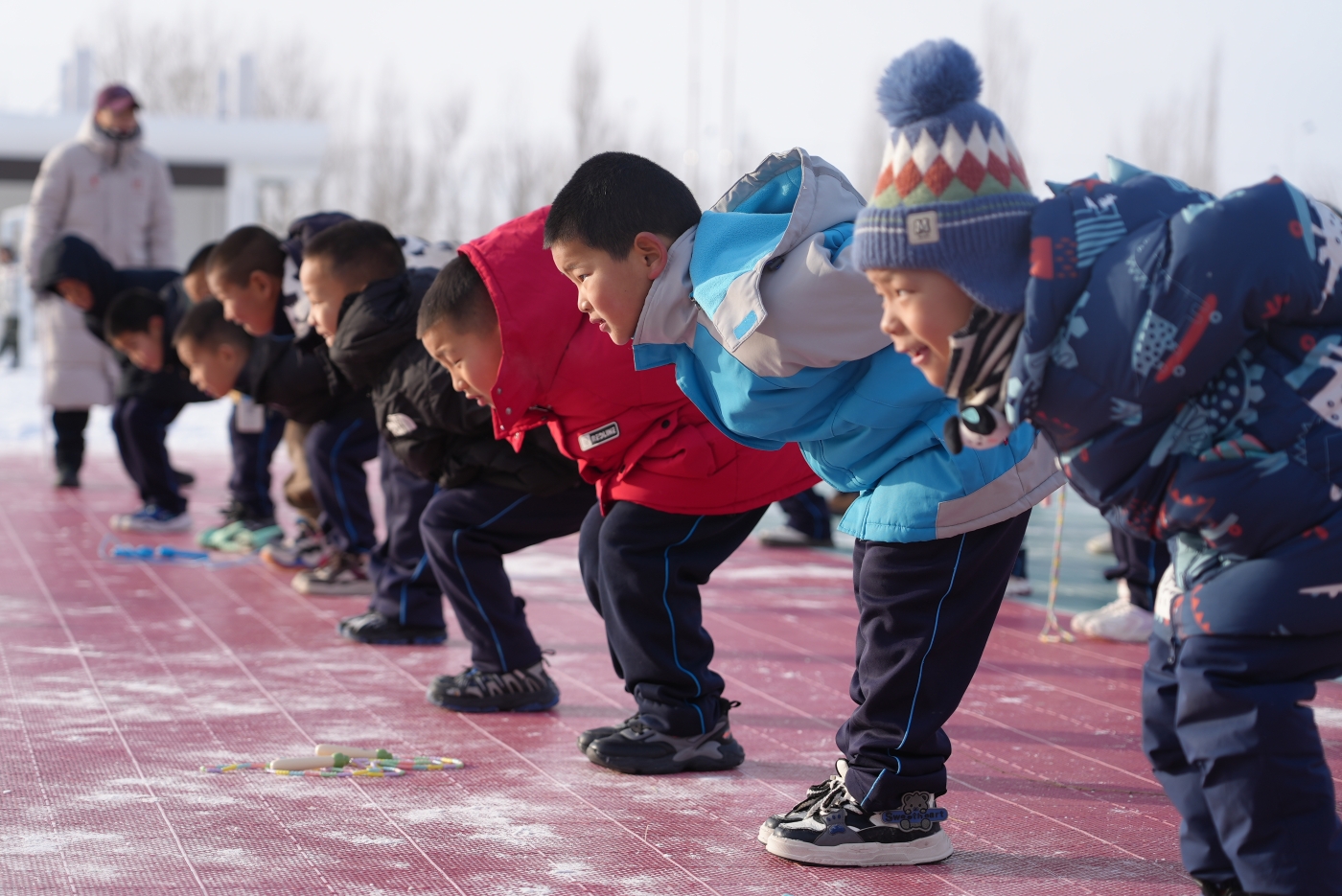 图2为：12月12日，新疆生产建设兵团第十师一八二团中学操场上，一年级小学生正在佳木斯援疆老师的指导下进行速滑运动基础练习。谢国庆摄