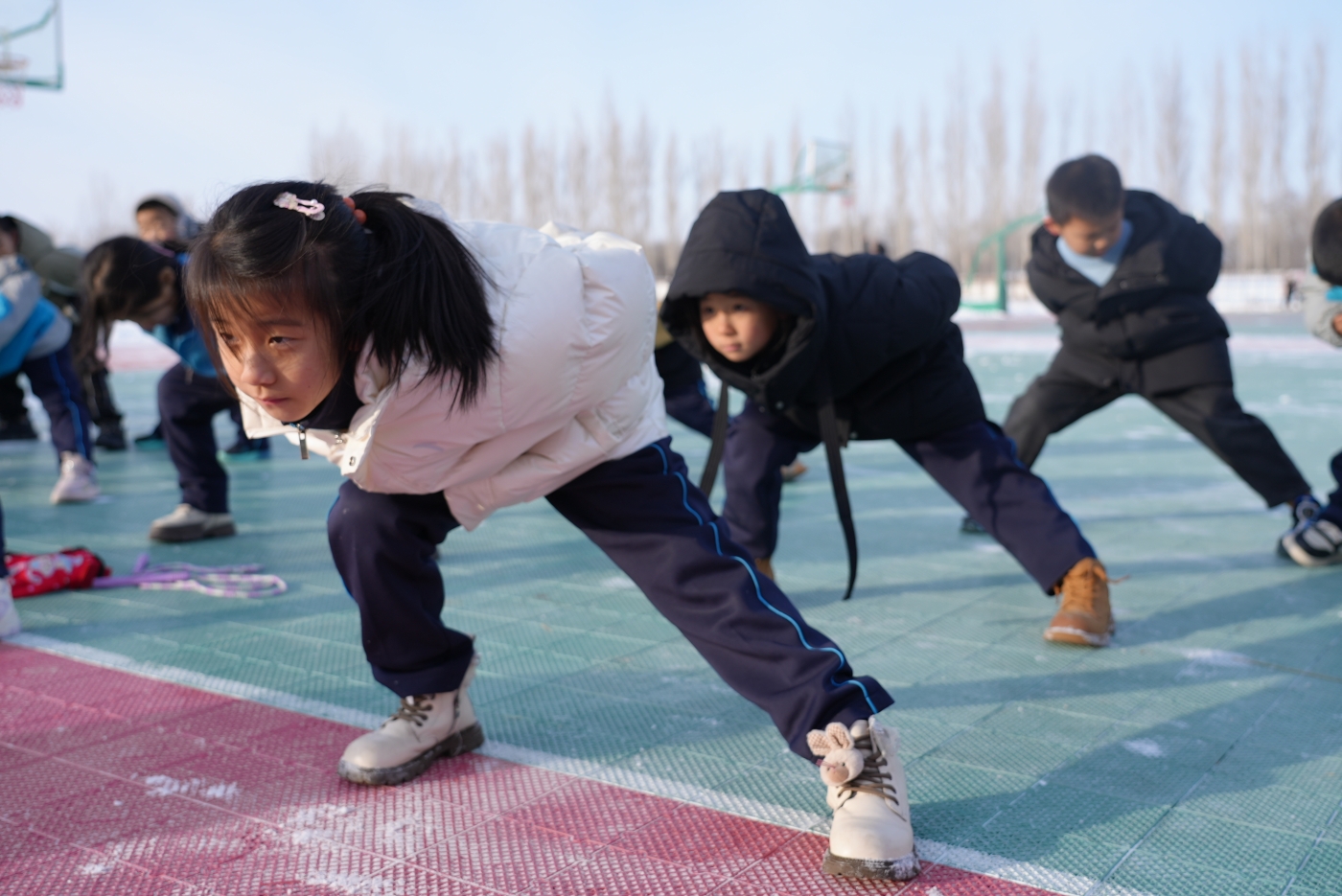 图1为：12月12日，新疆生产建设兵团第十师一八二团中学操场上，一年级小学生正在佳木斯援疆老师的指导下进行速滑运动基础练习。谢国庆摄